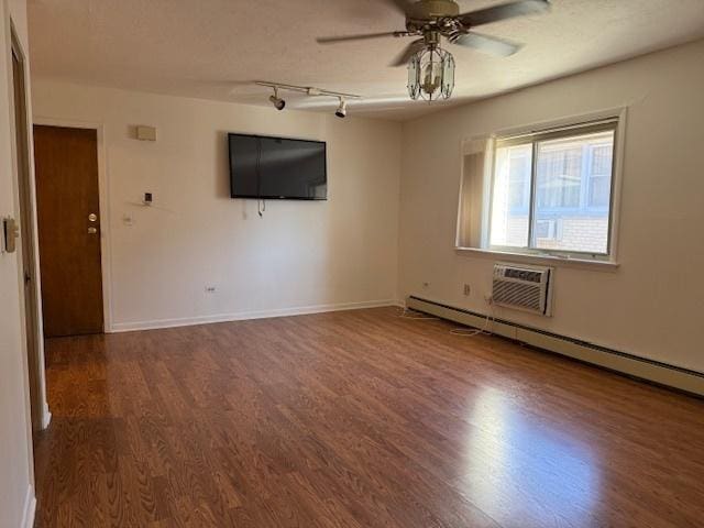 spare room featuring a wall unit AC, a baseboard heating unit, wood finished floors, a ceiling fan, and baseboards