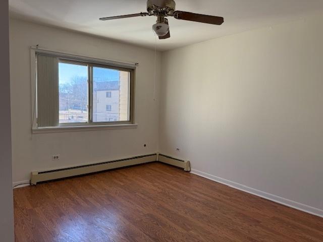 unfurnished room with a ceiling fan, baseboards, baseboard heating, and wood finished floors