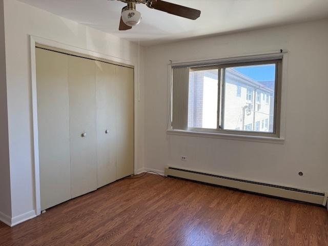 unfurnished bedroom featuring a closet, a baseboard radiator, wood finished floors, and a ceiling fan