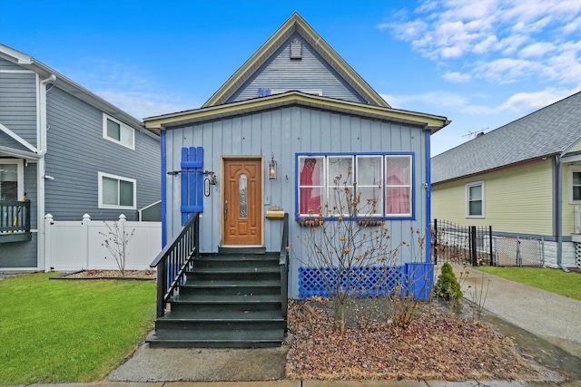 view of front of home with entry steps, board and batten siding, a front yard, and fence