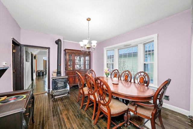 dining room with dark wood-style flooring, an inviting chandelier, a wood stove, and baseboards