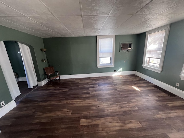 unfurnished room featuring arched walkways, a healthy amount of sunlight, and wood finished floors