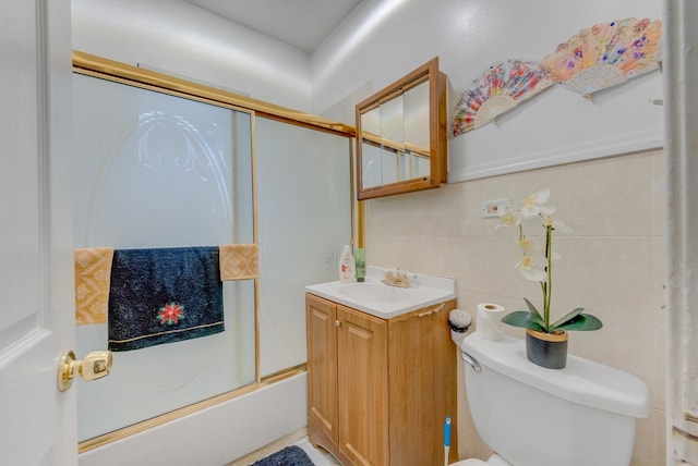 bathroom featuring toilet, enclosed tub / shower combo, tile walls, and vanity