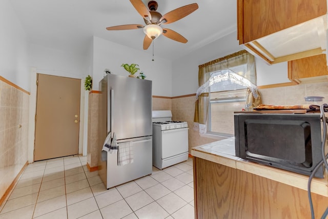 kitchen with light tile patterned floors, freestanding refrigerator, white gas range, black microwave, and tile walls