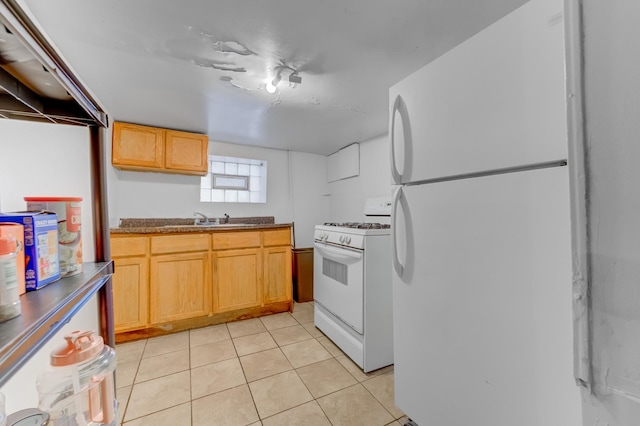 kitchen featuring dark countertops, white appliances, light tile patterned floors, and a sink