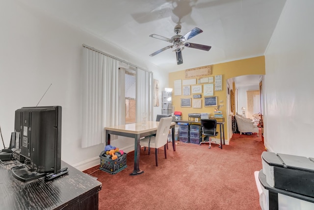 carpeted office featuring arched walkways, ceiling fan, crown molding, and baseboards