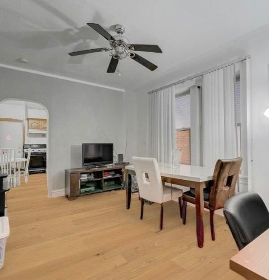 dining space with arched walkways, light wood finished floors, crown molding, and ceiling fan