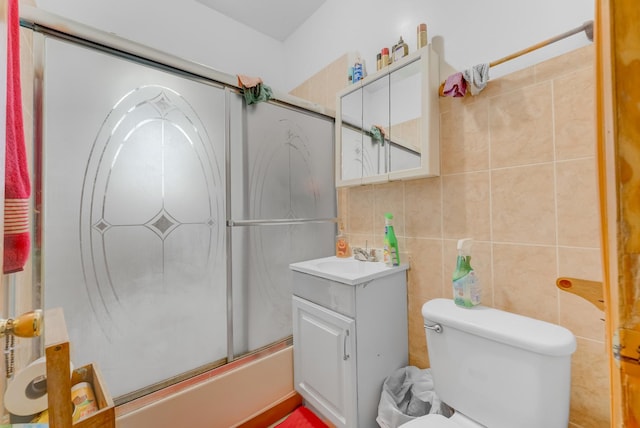 bathroom featuring vanity, toilet, combined bath / shower with glass door, tile walls, and backsplash
