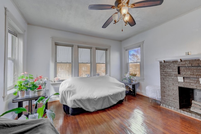 bedroom featuring a brick fireplace, ceiling fan, a textured ceiling, and wood finished floors