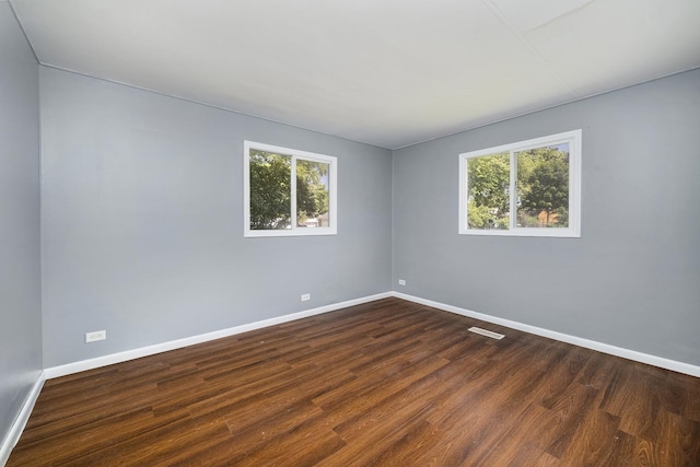 unfurnished room with a healthy amount of sunlight, baseboards, and dark wood-type flooring