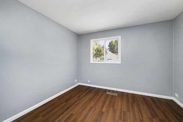 empty room featuring dark wood-style floors, visible vents, and baseboards