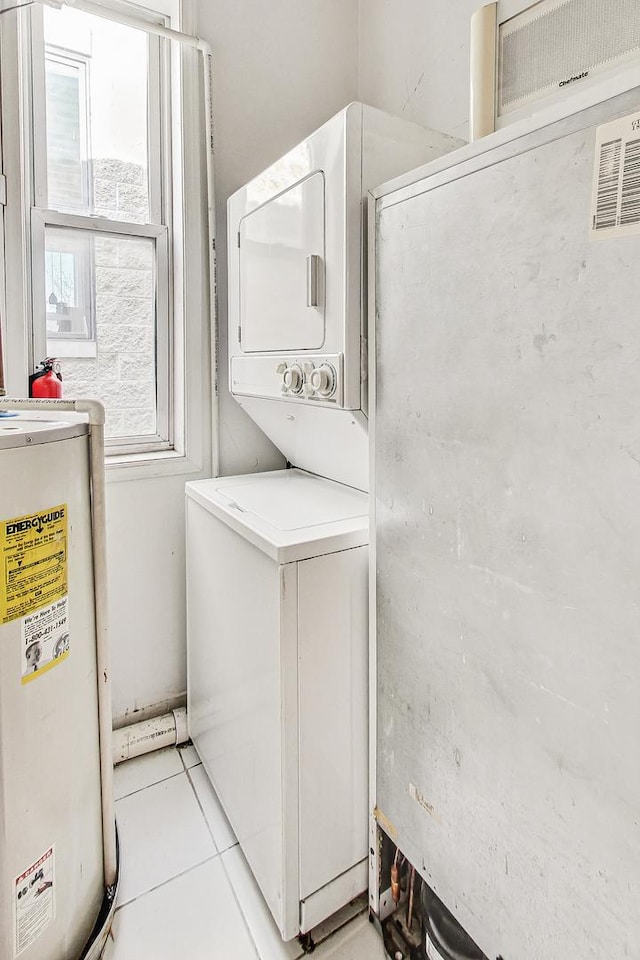 clothes washing area featuring water heater, stacked washing maching and dryer, and light tile patterned flooring