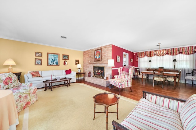 living room featuring visible vents, a notable chandelier, wood finished floors, crown molding, and a brick fireplace