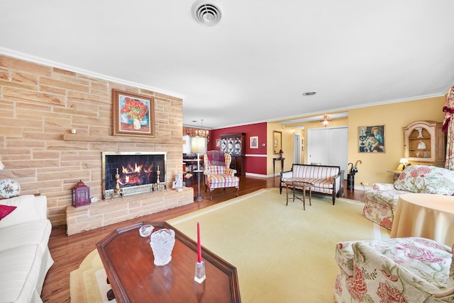 living area featuring visible vents, wood finished floors, a stone fireplace, crown molding, and baseboards