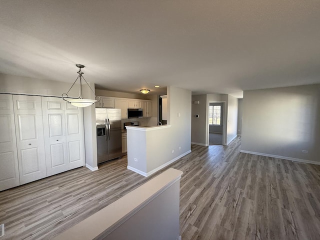 kitchen featuring baseboards, white cabinets, appliances with stainless steel finishes, open floor plan, and wood finished floors