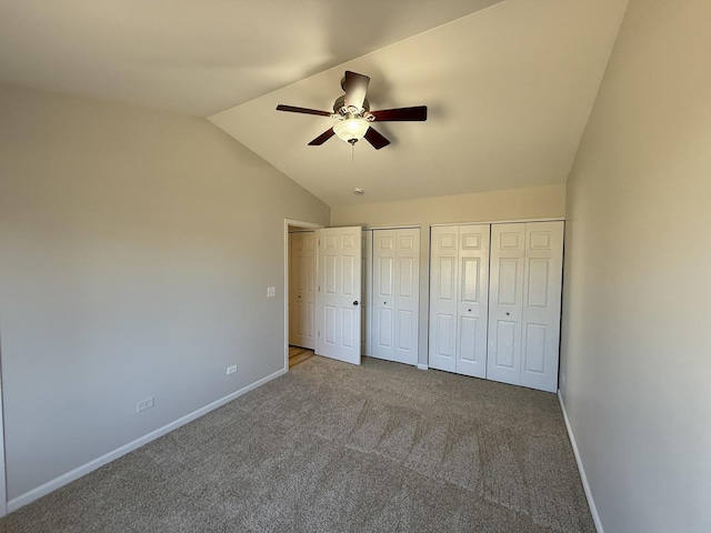 unfurnished bedroom featuring carpet, baseboards, vaulted ceiling, and two closets