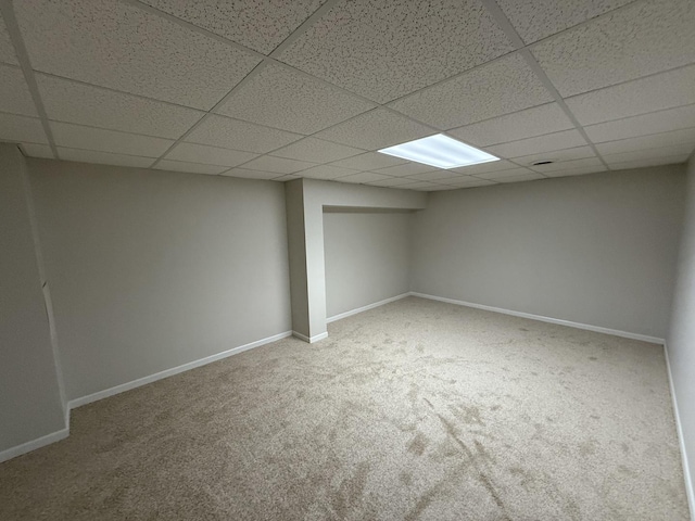 finished below grade area featuring carpet flooring, a drop ceiling, and baseboards