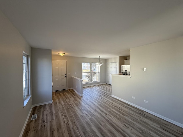 unfurnished living room with baseboards, visible vents, and dark wood-style flooring