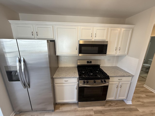 kitchen with light wood finished floors, white cabinets, light stone counters, stainless steel appliances, and backsplash