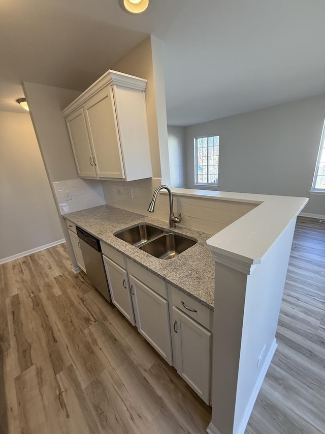 kitchen with tasteful backsplash, dishwasher, a peninsula, light wood-type flooring, and a sink