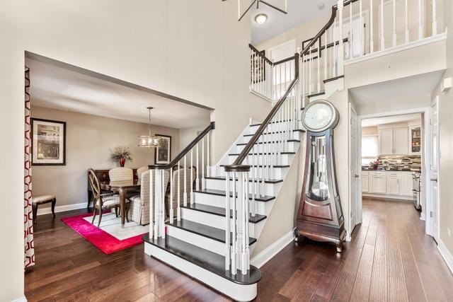 stairs with a towering ceiling, an inviting chandelier, baseboards, and hardwood / wood-style floors