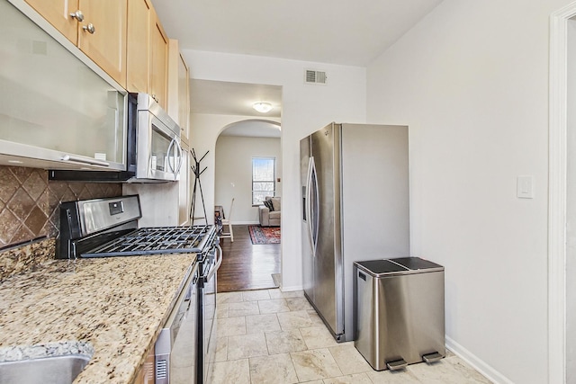 kitchen with tasteful backsplash, visible vents, arched walkways, light stone counters, and stainless steel appliances