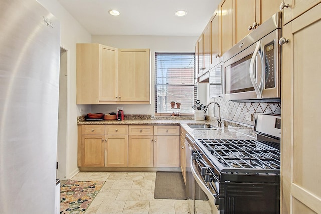 kitchen with light stone counters, stainless steel appliances, backsplash, light brown cabinetry, and a sink