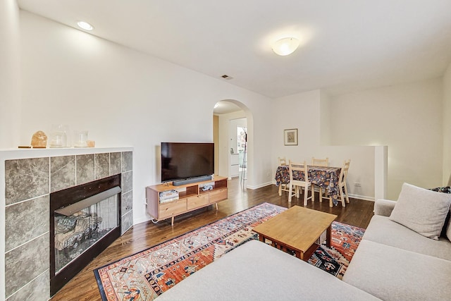 living room featuring arched walkways, a fireplace, wood finished floors, visible vents, and baseboards