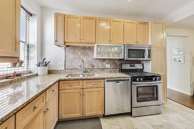 kitchen featuring light stone counters, light brown cabinets, stainless steel appliances, a sink, and decorative backsplash