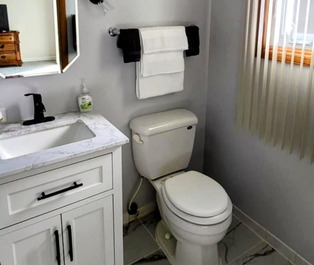 half bathroom featuring marble finish floor, baseboards, vanity, and toilet