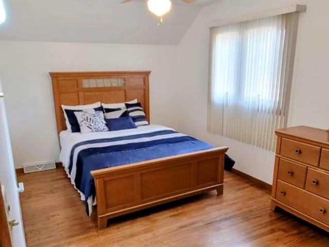 bedroom with vaulted ceiling, light wood-style flooring, visible vents, and a ceiling fan