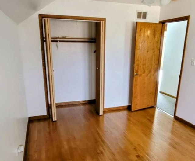 unfurnished bedroom featuring a closet, visible vents, baseboards, and wood finished floors