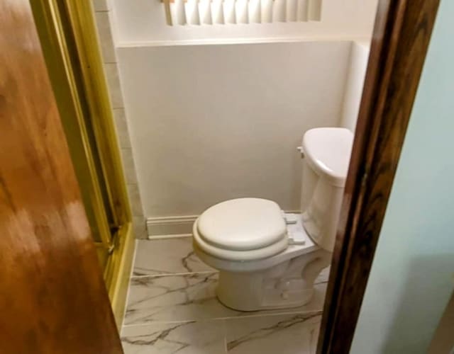 full bathroom with toilet, marble finish floor, baseboards, and walk in shower