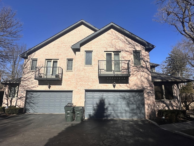 view of front of property with a garage, a balcony, aphalt driveway, and brick siding