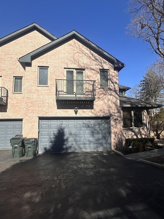 view of front of home with a balcony, driveway, an attached garage, and brick siding