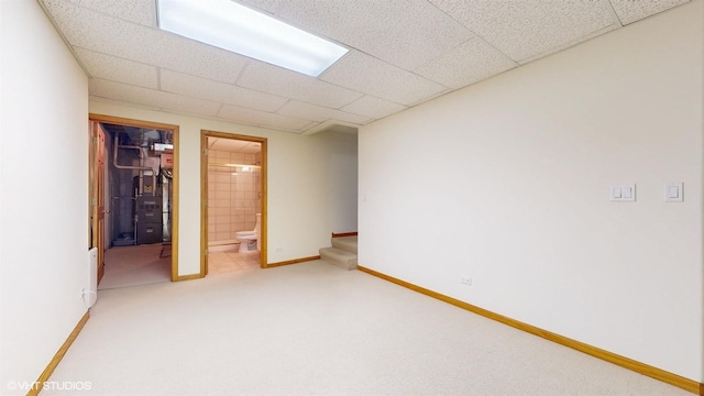 interior space featuring carpet, a spacious closet, ensuite bath, a drop ceiling, and baseboards