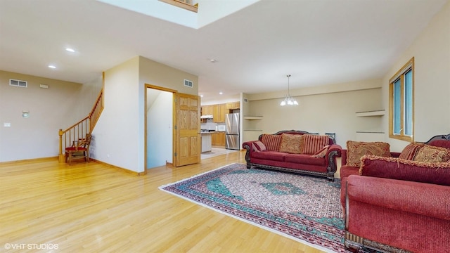 living room featuring light wood-style flooring, stairs, visible vents, and a notable chandelier