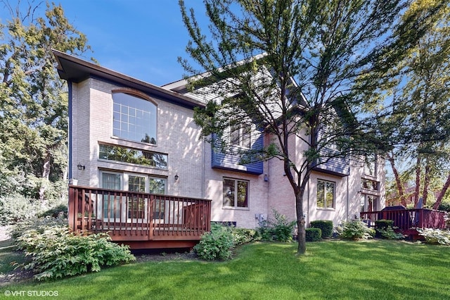 back of house with a deck, brick siding, and a lawn