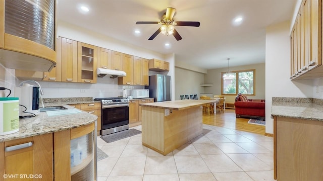 kitchen featuring light tile patterned floors, under cabinet range hood, appliances with stainless steel finishes, a center island, and tasteful backsplash