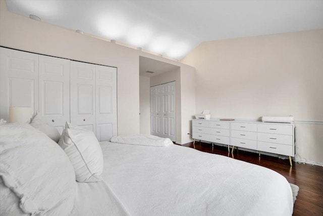 bedroom with multiple closets, dark wood finished floors, and vaulted ceiling