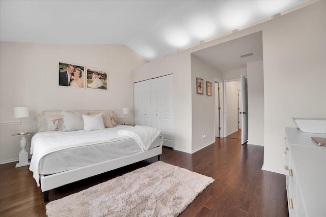 bedroom with visible vents, dark wood-style floors, a closet, baseboards, and vaulted ceiling