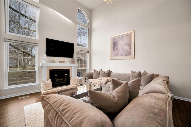 living area featuring wood finished floors, visible vents, baseboards, a high ceiling, and a tile fireplace