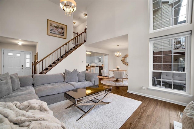 living area featuring baseboards, an inviting chandelier, stairs, dark wood-type flooring, and a towering ceiling