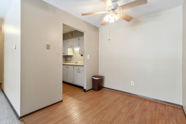 interior space featuring light countertops, light wood-style flooring, a ceiling fan, white cabinets, and baseboards