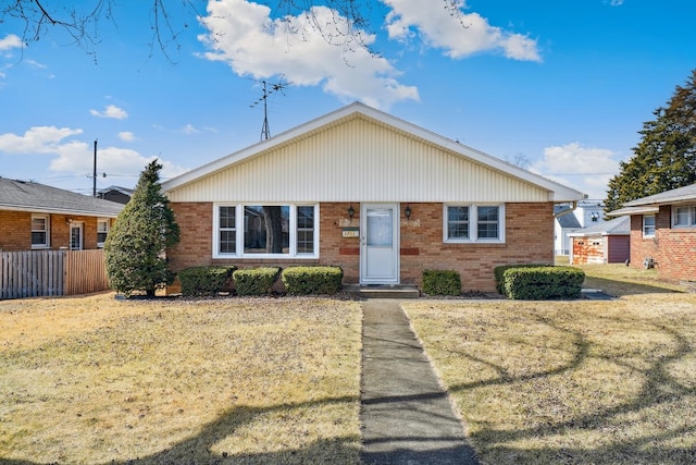 view of front facade with brick siding, a front lawn, and fence