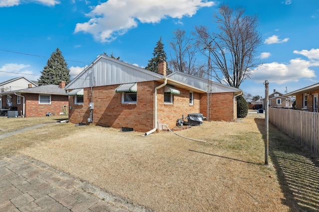 back of house featuring a lawn, fence, cooling unit, brick siding, and a chimney