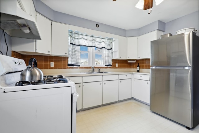 kitchen featuring white gas stove, under cabinet range hood, a sink, freestanding refrigerator, and light countertops