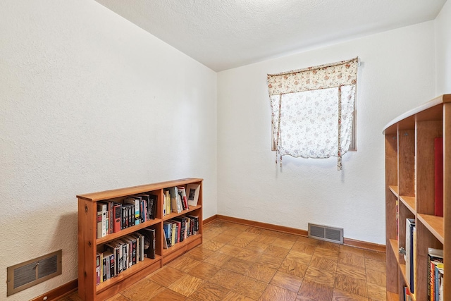 interior space with visible vents, baseboards, a textured ceiling, and a textured wall