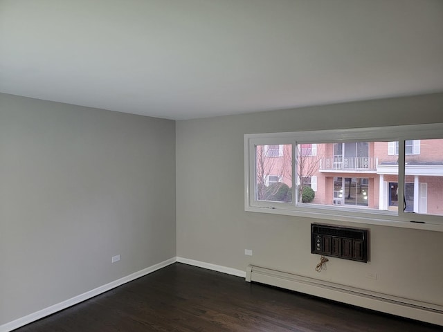 spare room featuring a wealth of natural light, dark wood-type flooring, a baseboard heating unit, and baseboards