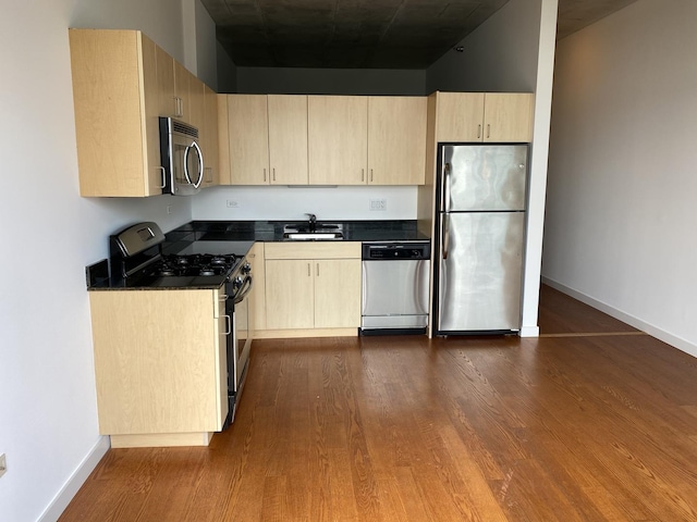 kitchen with stainless steel appliances, dark countertops, light brown cabinets, and a sink